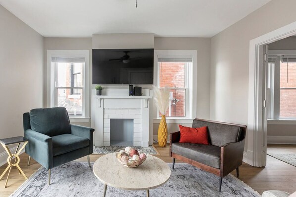 A living room with a fireplace, two sofas, a coffee table, and a TV mounted above the fireplace.