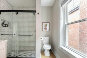 A bathroom with a shower, toilet, and a window with a brick wall view. - Newly Renovated 2BR Apartment w/ Free Parking in Downtown (Lexington)