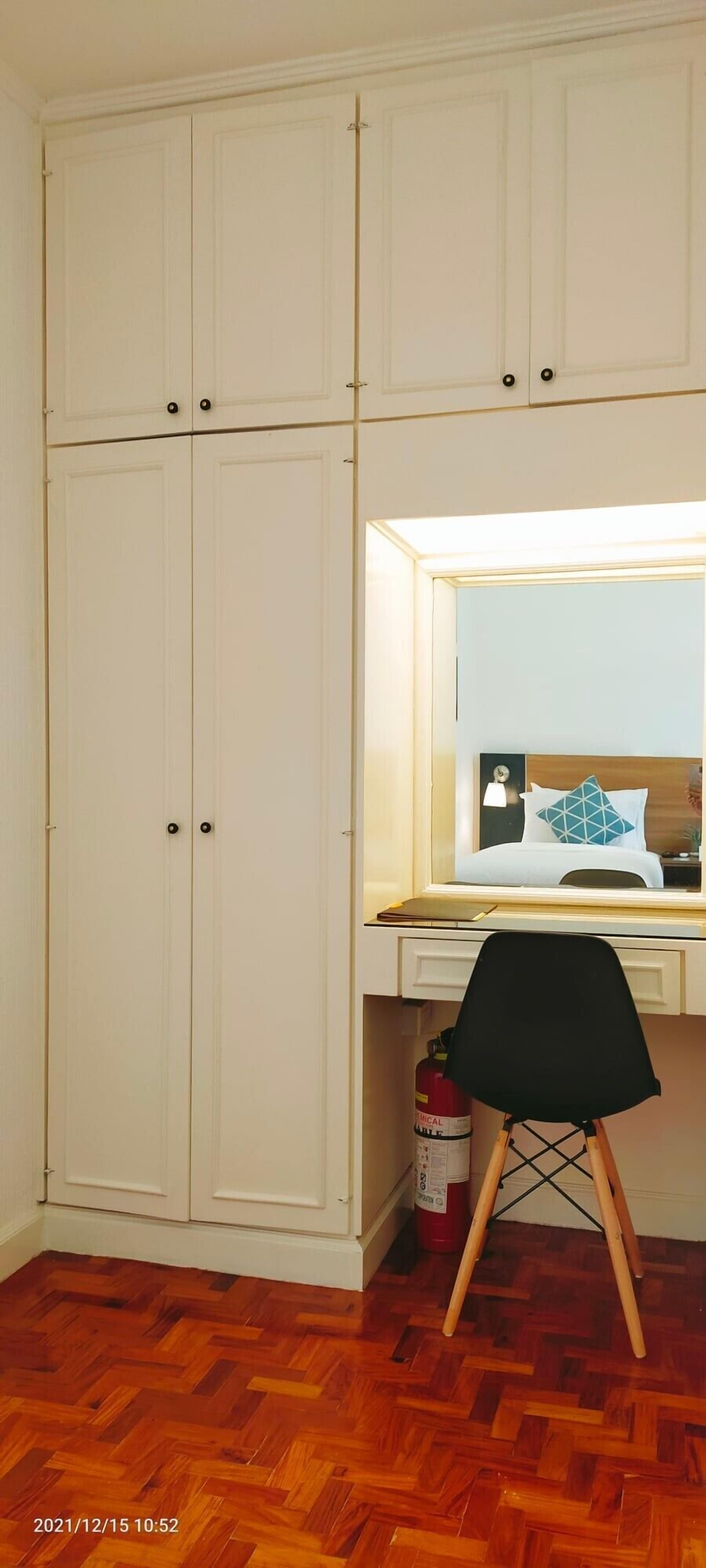 Una habitación con piso de madera en patrón chevron, un escritorio con espejo, una silla negra y un extintor.