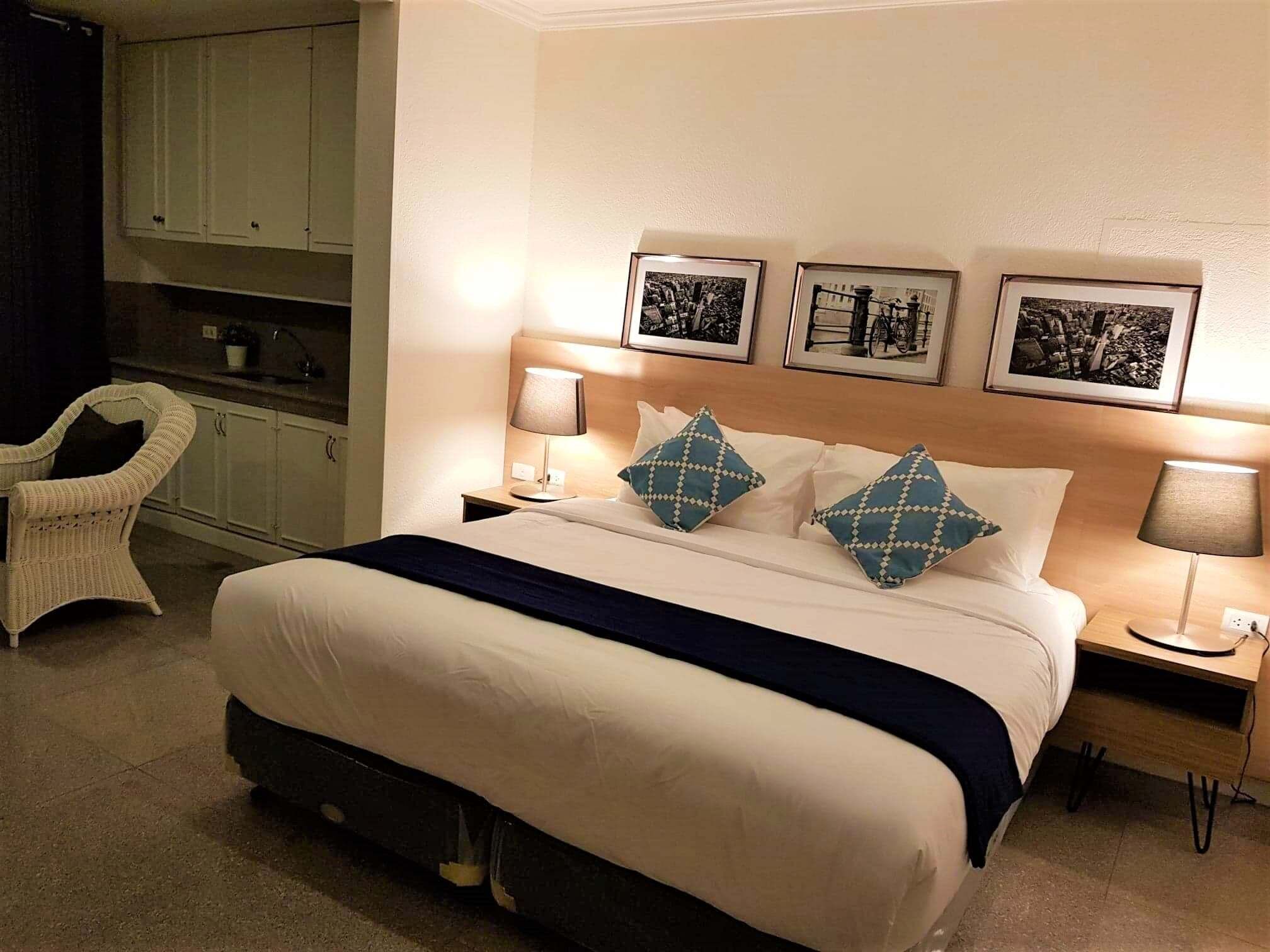 Een hotelkamer met een bed, twee nachtkastjes, een stoel en een kitchenette.