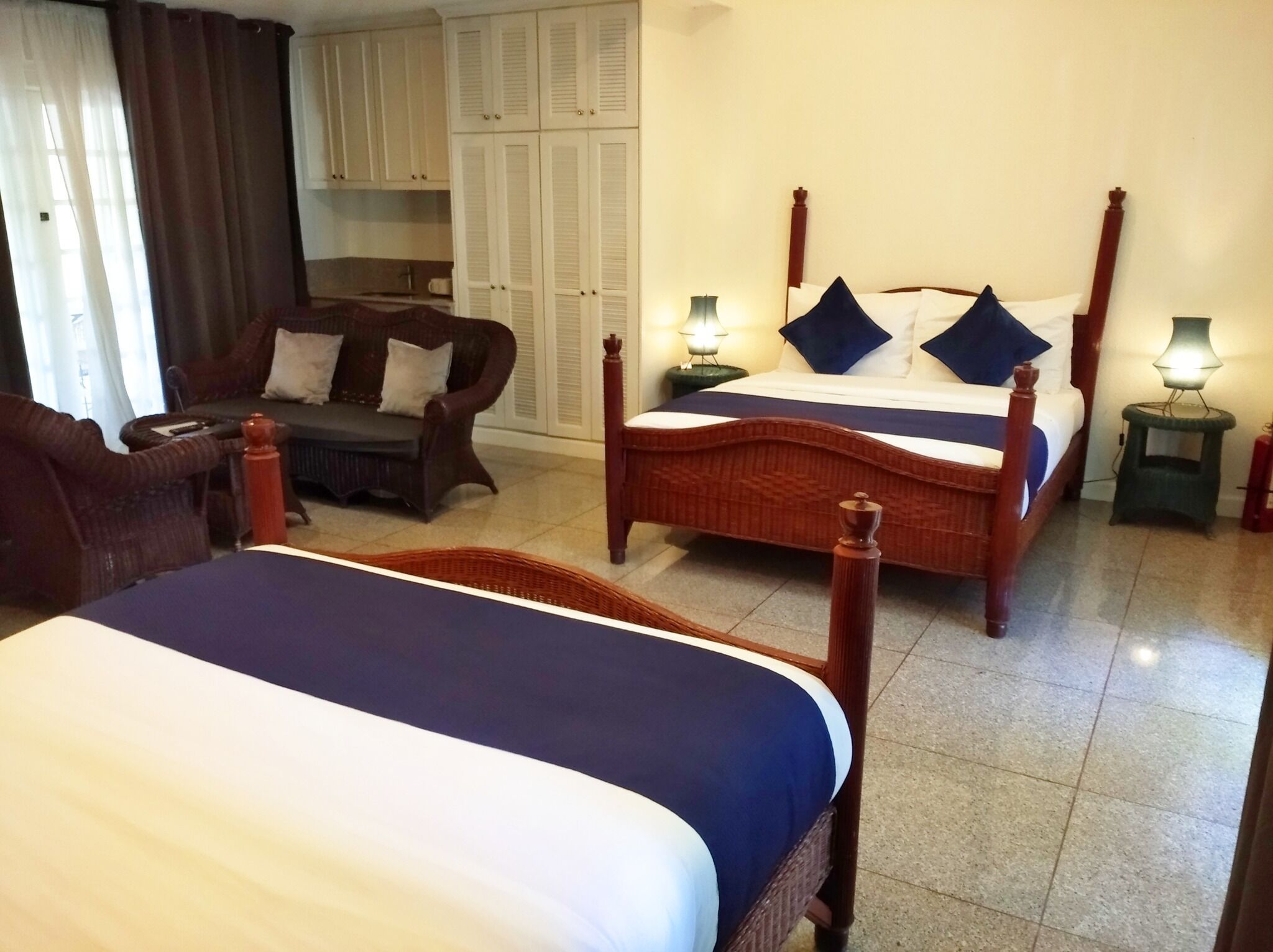 A hotel room with two beds, a sofa, a wardrobe, and two nightstands with lamps.