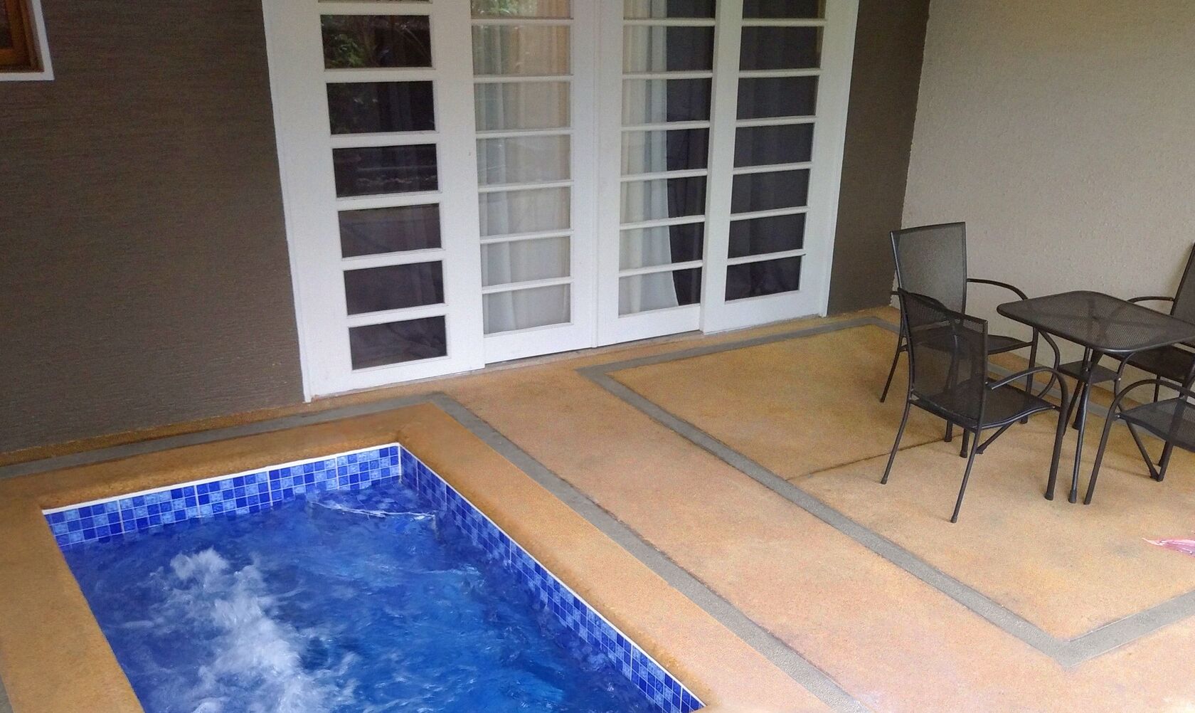 A hot tub in a covered outdoor area with a table and chairs nearby.