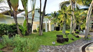 Un jardín tropical con palmeras, un sendero de piedra y un edificio de fachada blanca.