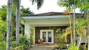 Una casa con porche cubierto, sendero de piedra y vegetación tropical.