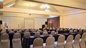 A conference room with rows of tables and chairs, a podium, and a large chandelier.