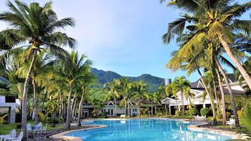 A resort pool surrounded by palm trees and houses with a mountain in the background.