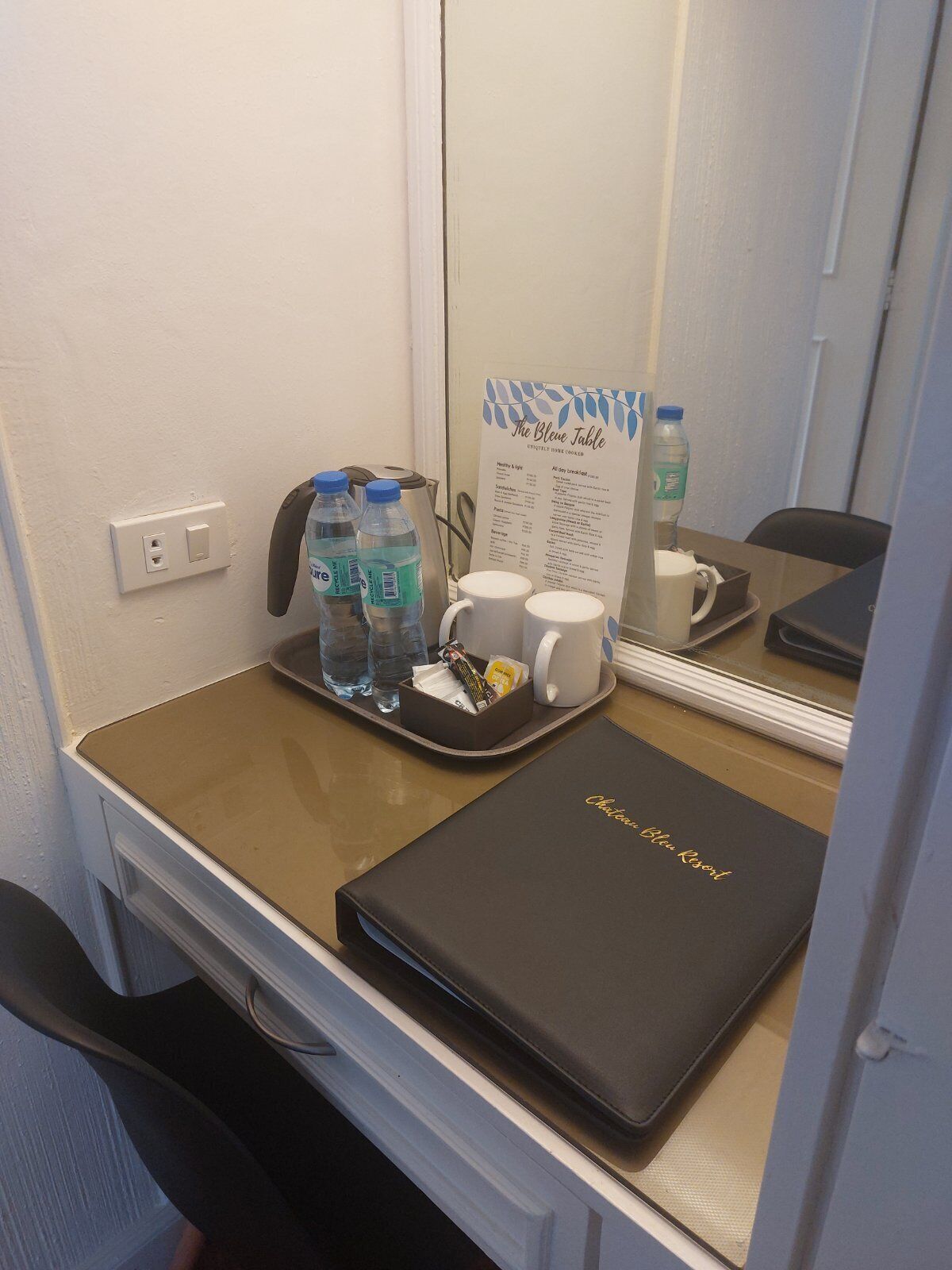 A hotel room with a desk, a tray with water bottles, a coffee maker, and a menu.