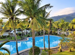 A swimming pool surrounded by palm trees and white buildings with thatched roofs. - Chateau Bleu Resort (Calamba)