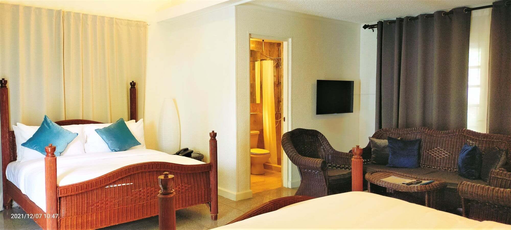 Ett hotellrum med en säng, en soffa, en stol, en tv och ett badrum som syns genom en öppen dörr.