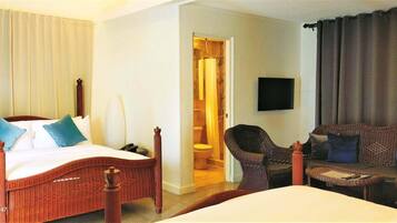Habitación de hotel con cama, sofá, silla, televisión y baño visible a través de una puerta abierta.