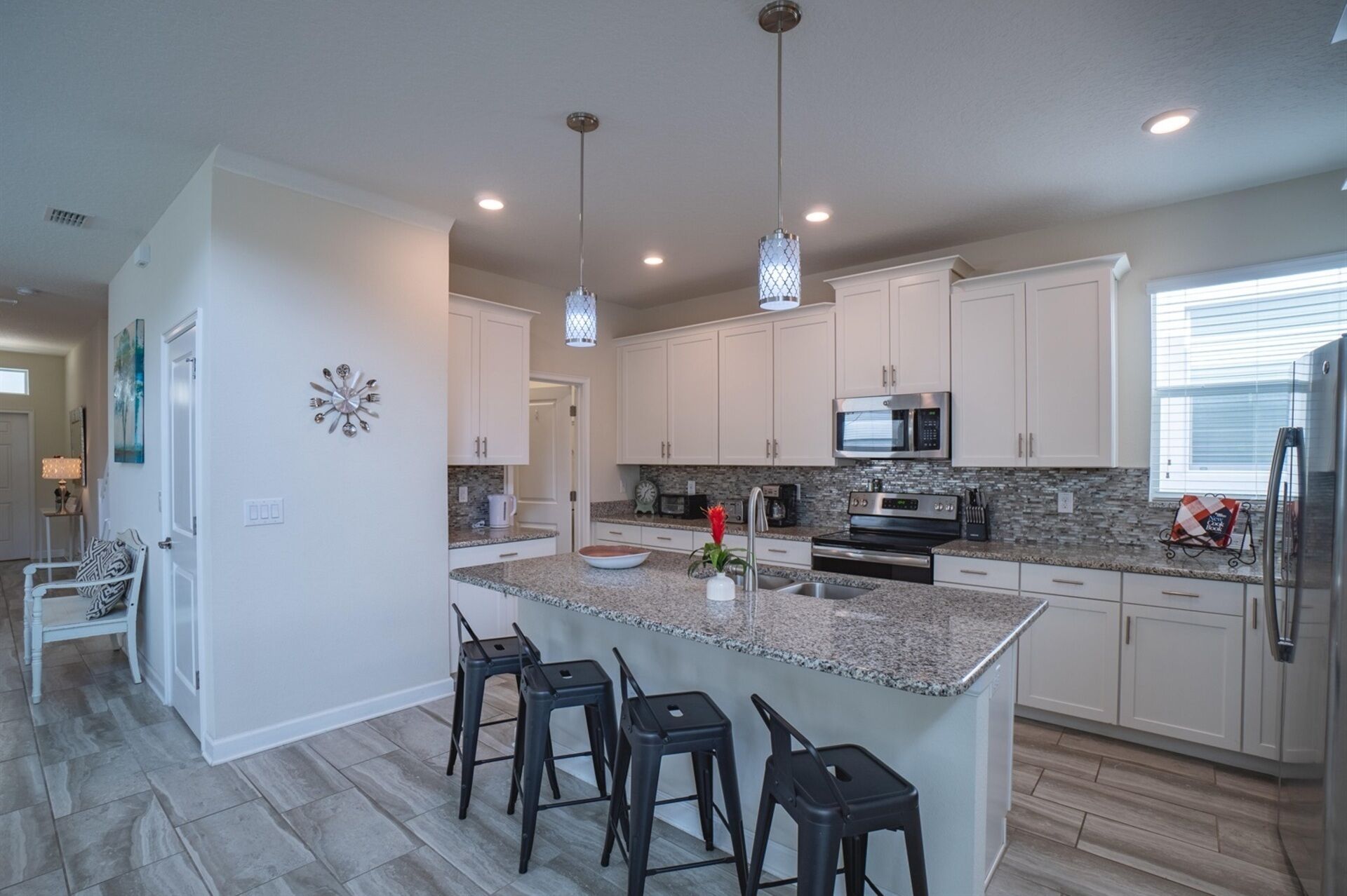 A modern kitchen with white cabinets, granite countertops, a central island with bar stools, stainless steel appliances, and pendant lighting.