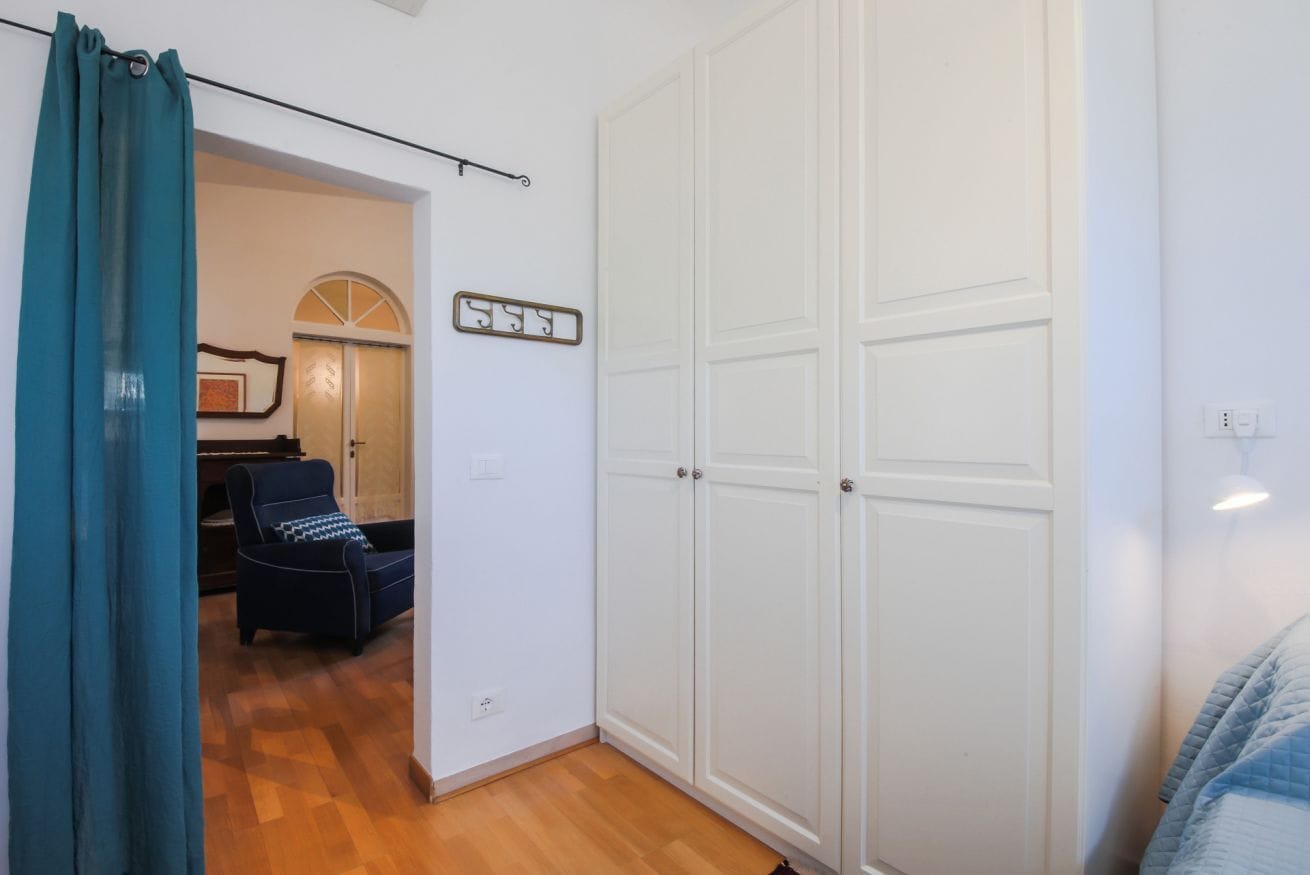 A room with a large white wardrobe, a blue armchair, and a piano in the background.