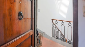 Eine Holztür mit Metallbeschlägen, eine Treppe mit schmiedeeisernen Geländern und eine Wand mit Lichtschalter.
