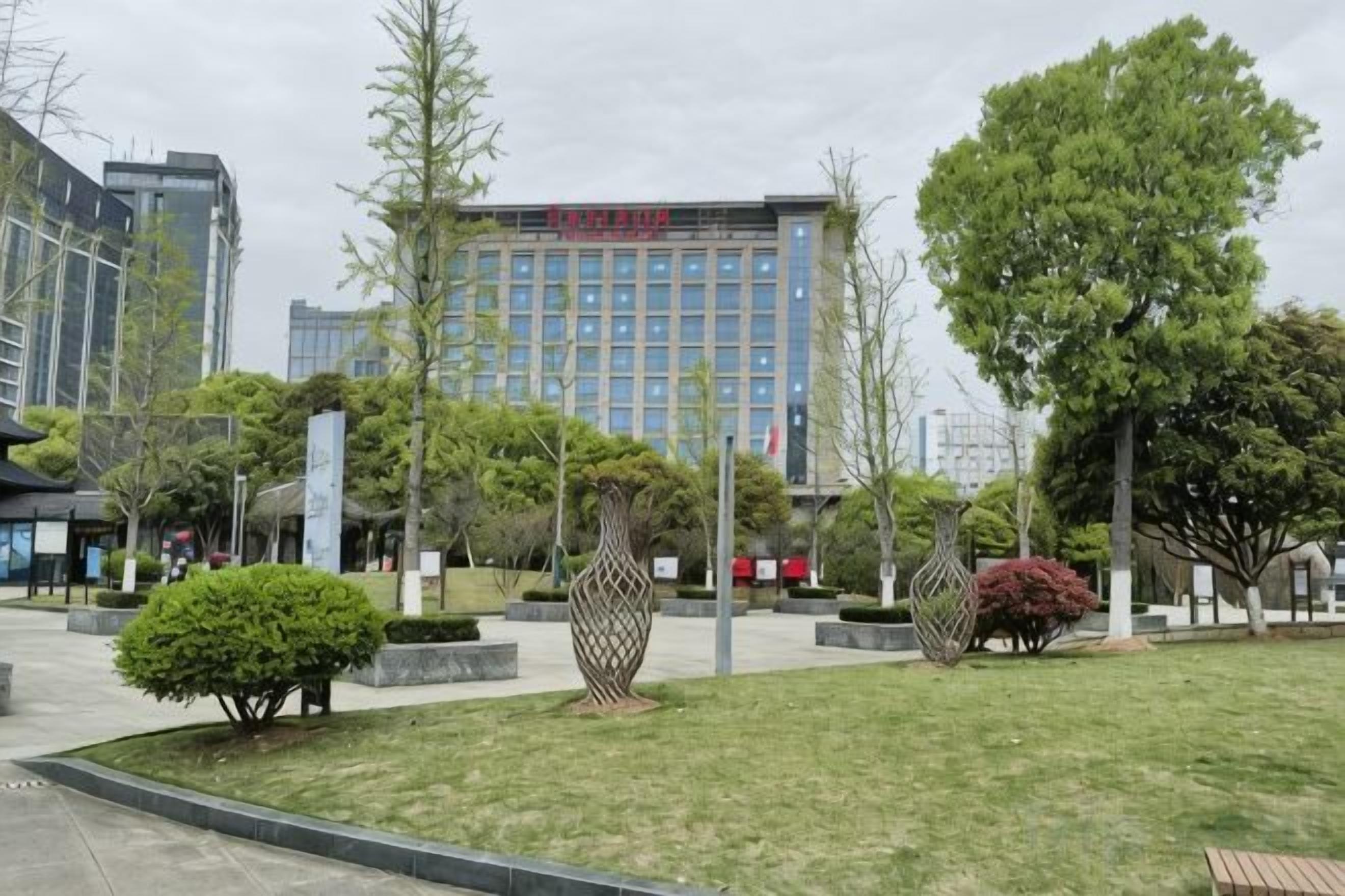 Zona ajardinada con un edificio al fondo, un sendero y diversas plantas y arbustos.