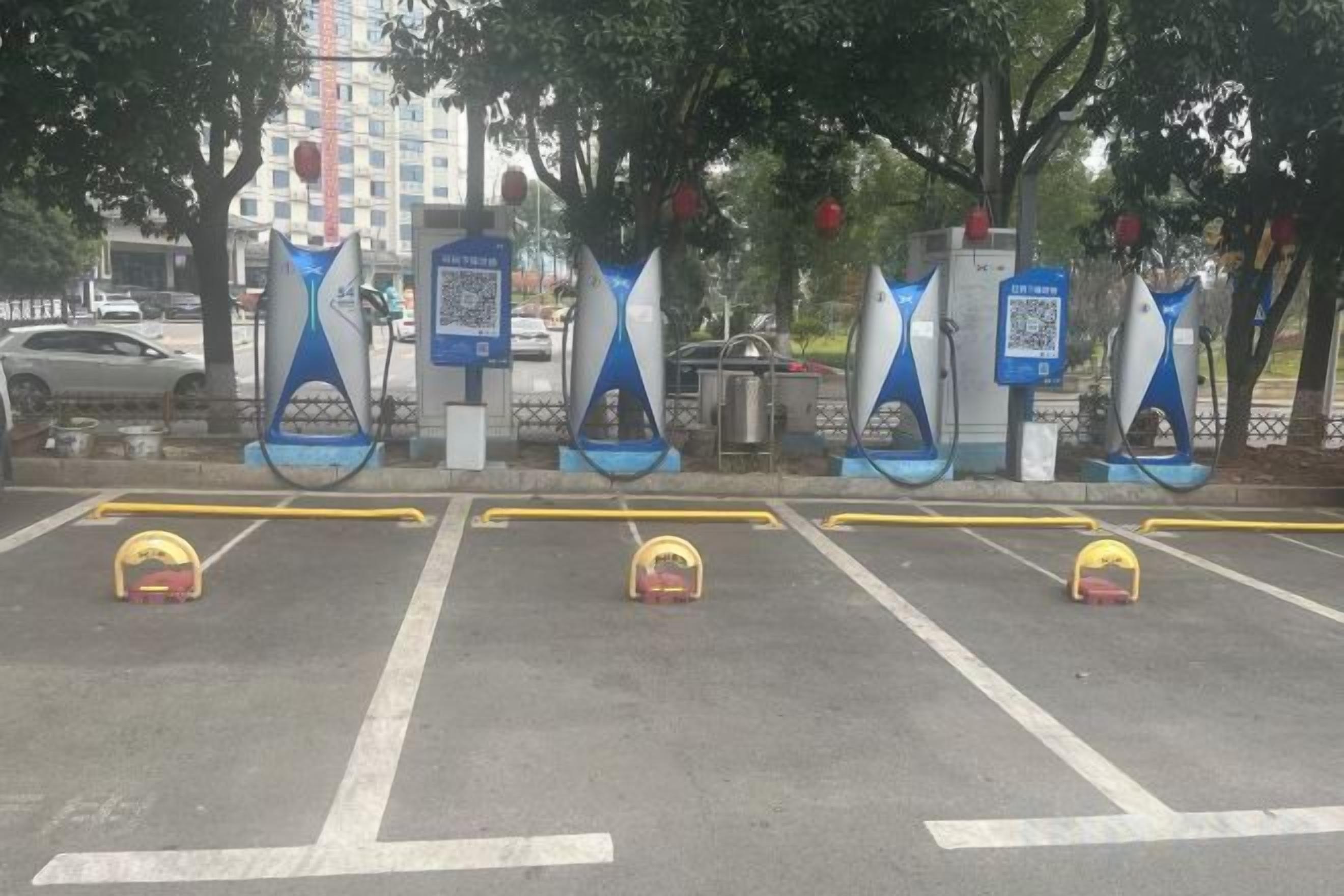 Un área de estacionamiento con estaciones de carga para vehículos eléctricos y un código QR para el pago.