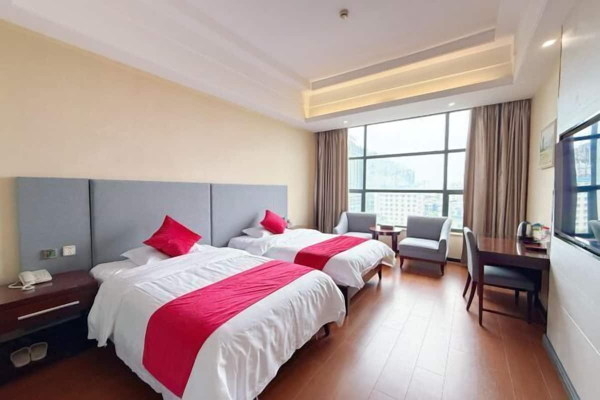 Une chambre d’hôtel avec deux lits, un bureau, une chaise et une grande fenêtre donnant sur la ville.
