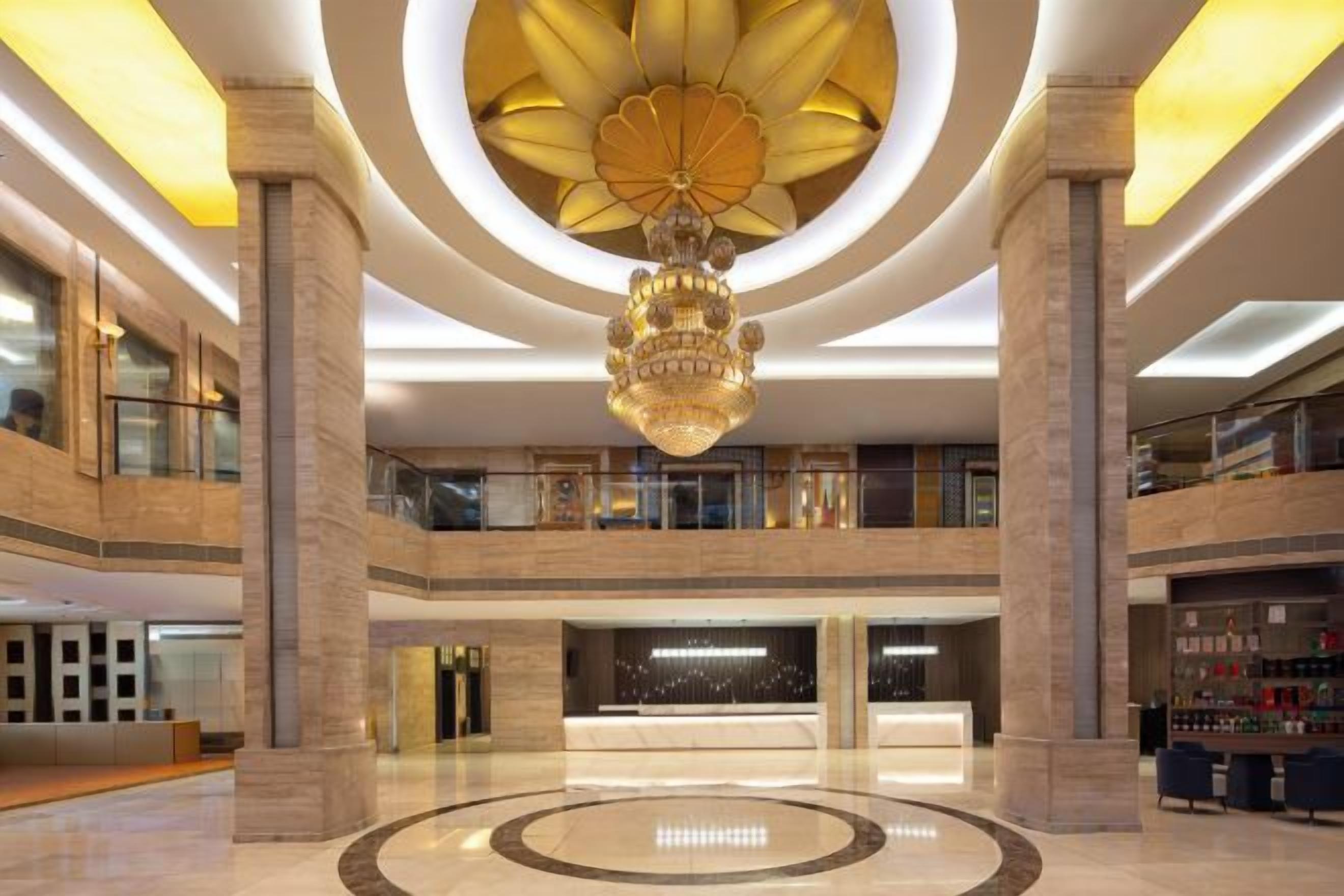 A spacious lobby with a grand chandelier, multiple levels, and a central circular design on the floor.