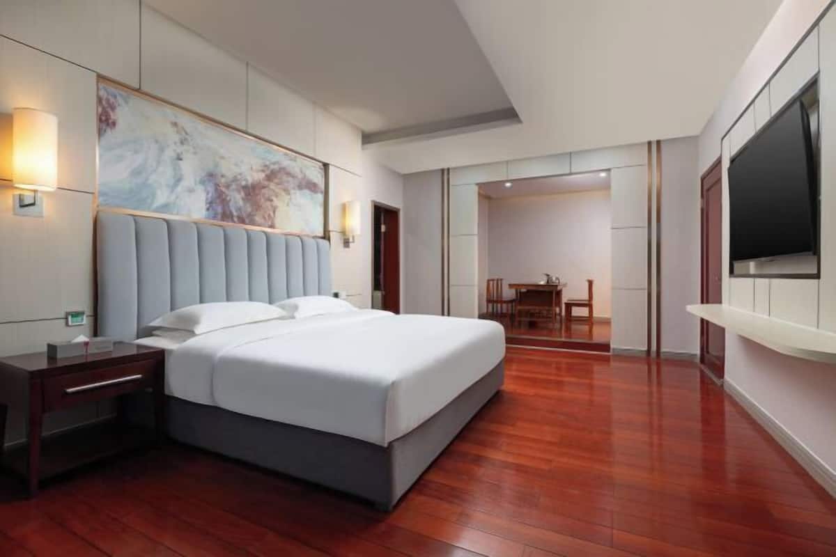 Une chambre d’hôtel moderne équipée d’un grand lit, d’un bureau, d’une chaise, d’un téléviseur à écran plat et d’un tableau au mur.