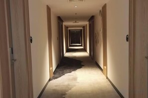 A hotel hallway with doors on both sides, a carpeted floor, and a light source at the end of the corridor.