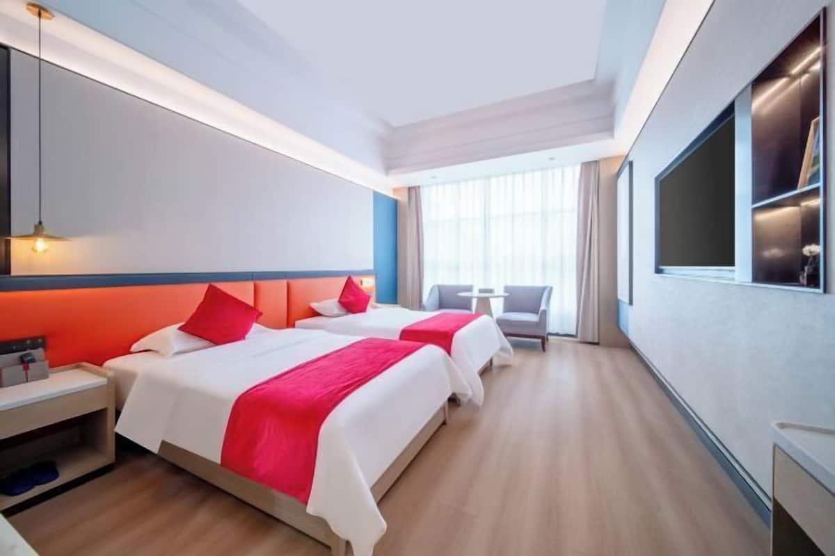 Une chambre d’hôtel avec deux lits, un bureau, une chaise, une télévision et une grande fenêtre.