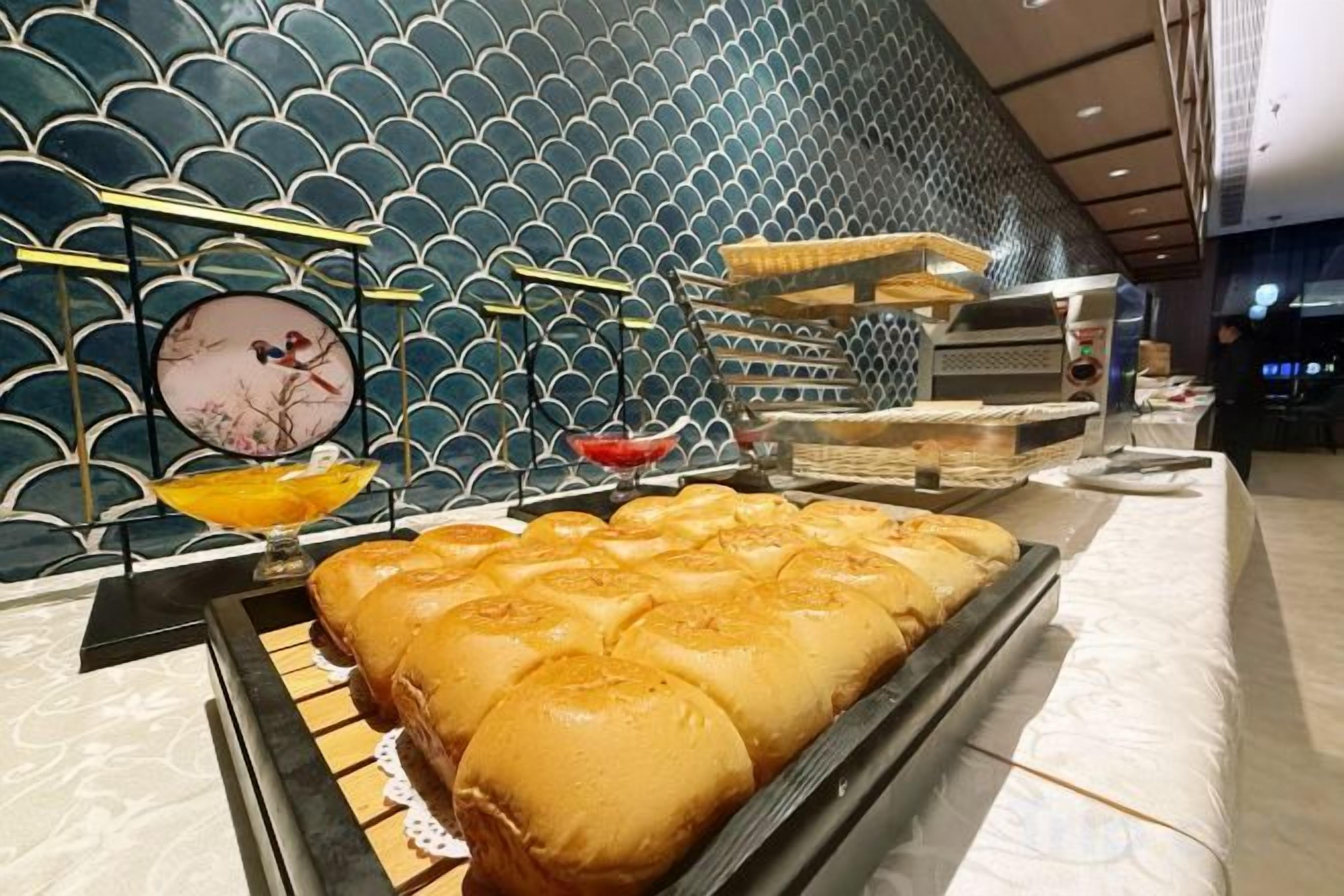 A buffet area with a variety of food items, including bread and pastries, and a decorative wall with a geometric pattern.
