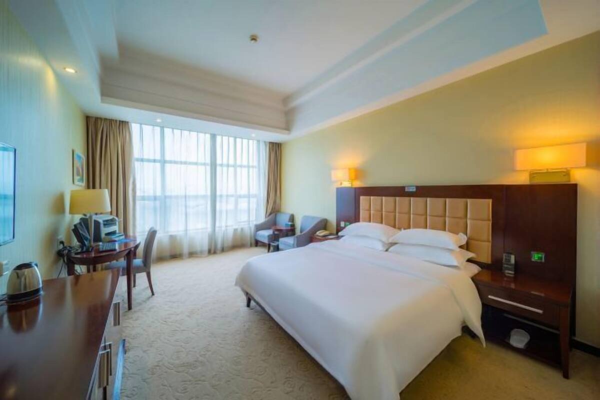 Ein Hotelzimmer mit einem großen Bett, einem Schreibtisch mit Stuhl, einem kleinen Tisch und einem Fernseher.
