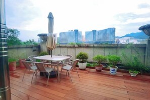 A rooftop terrace with a table and chairs, potted plants, and a view of city buildings.