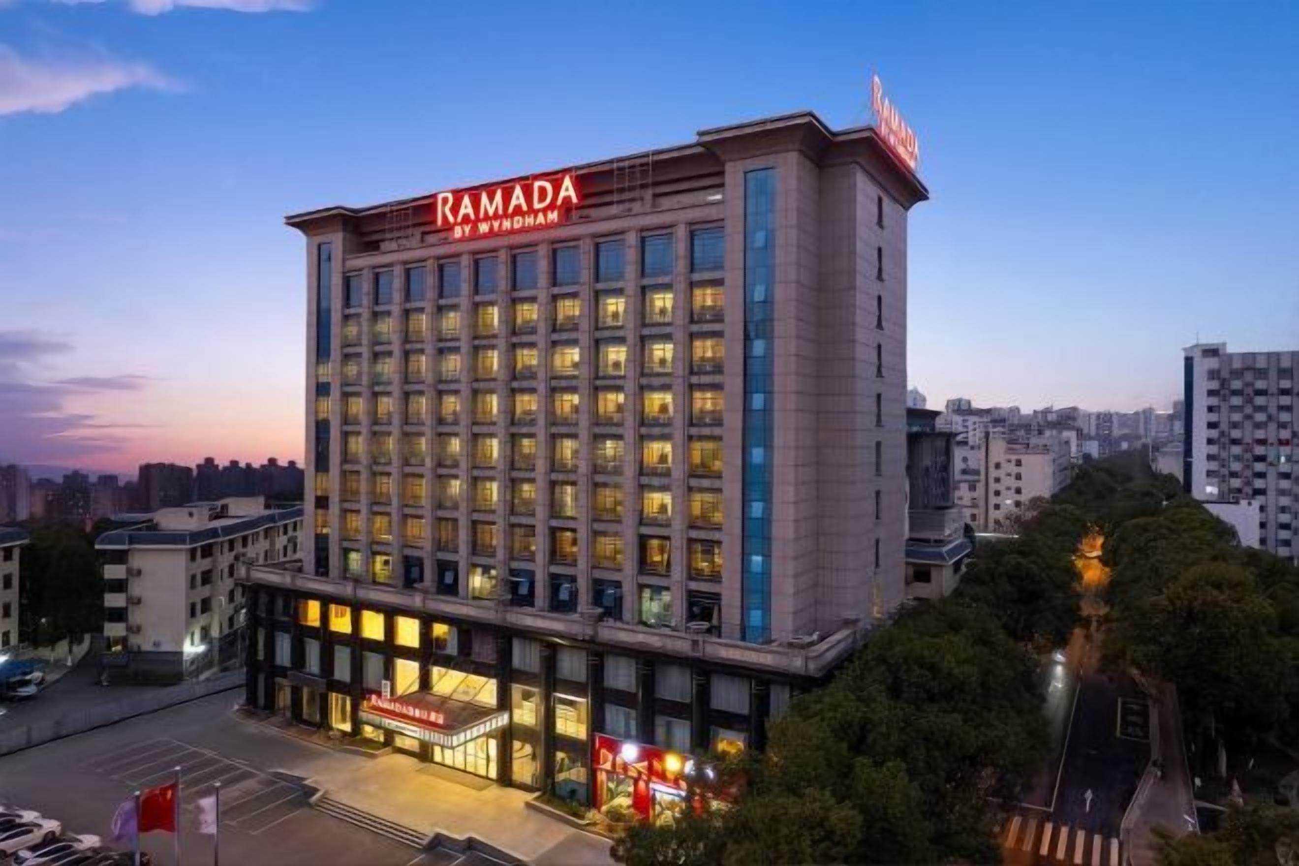 Un hotel de varios pisos con un llamativo letrero de 'RAMADA', que presenta un diseño arquitectónico moderno con techo plano y grandes ventanales.