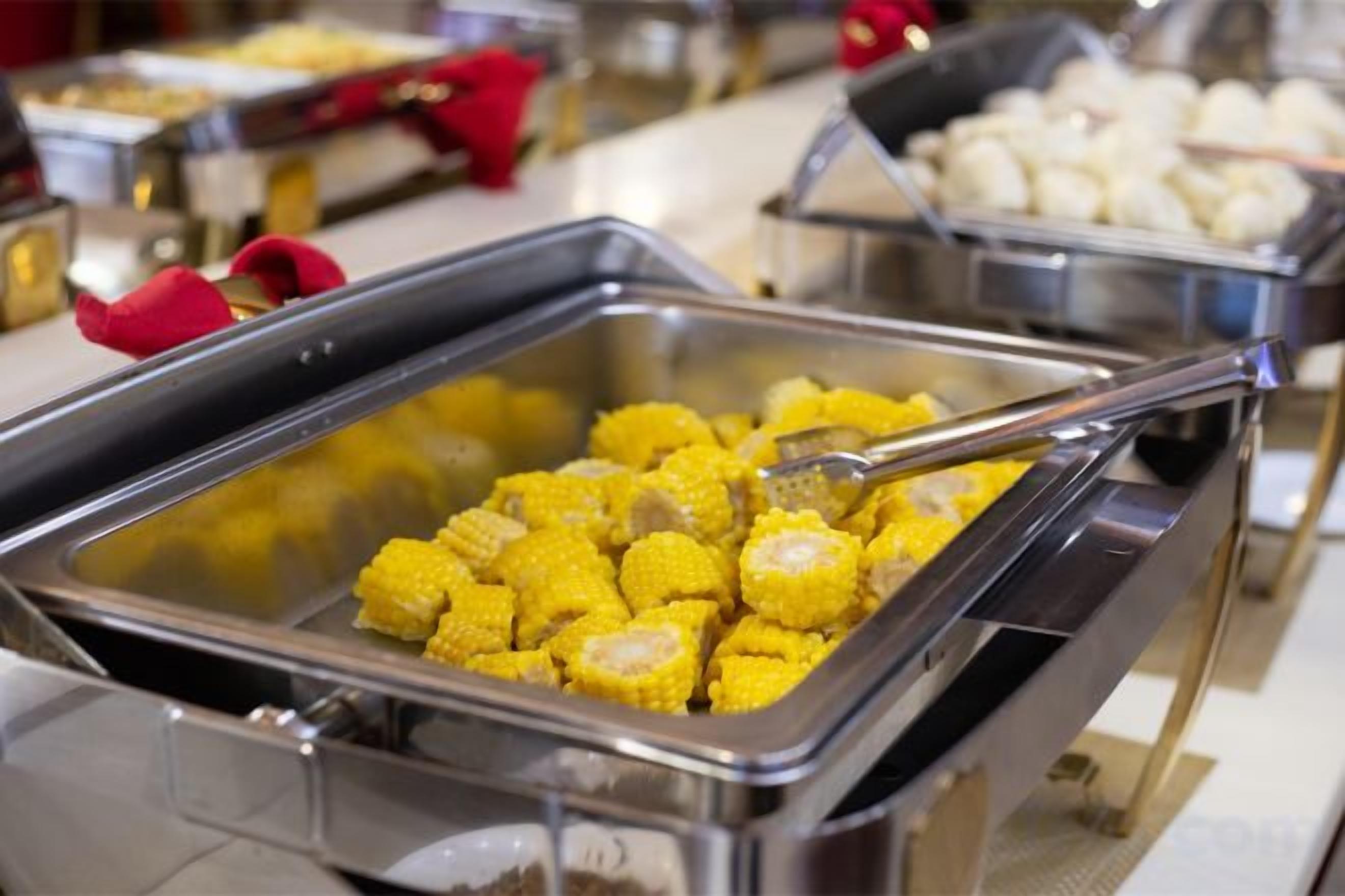 A buffet with various food items, including a container of corn and a container of what appears to be dumplings.