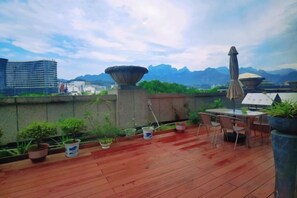 A rooftop terrace with potted plants, a table, chairs, and a view of mountains. - Ramada Hotel Zhangjiajie (Tianmen Mountain Cable Car Station) (Zhangjiajie)