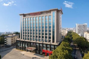 A multi-story hotel with a prominent 'RAMADA' sign, surrounded by other buildings and trees.