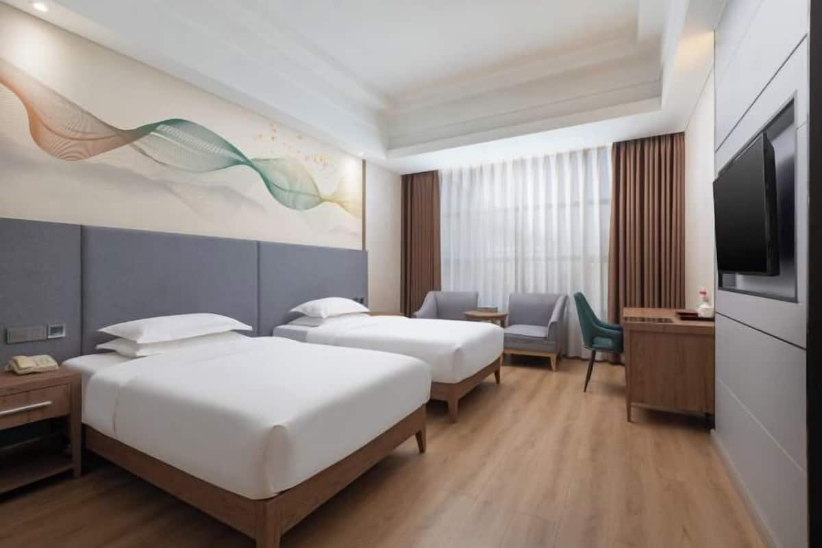 Une chambre d’hôtel avec deux lits, un bureau, une chaise, une télévision et un mur décoratif.