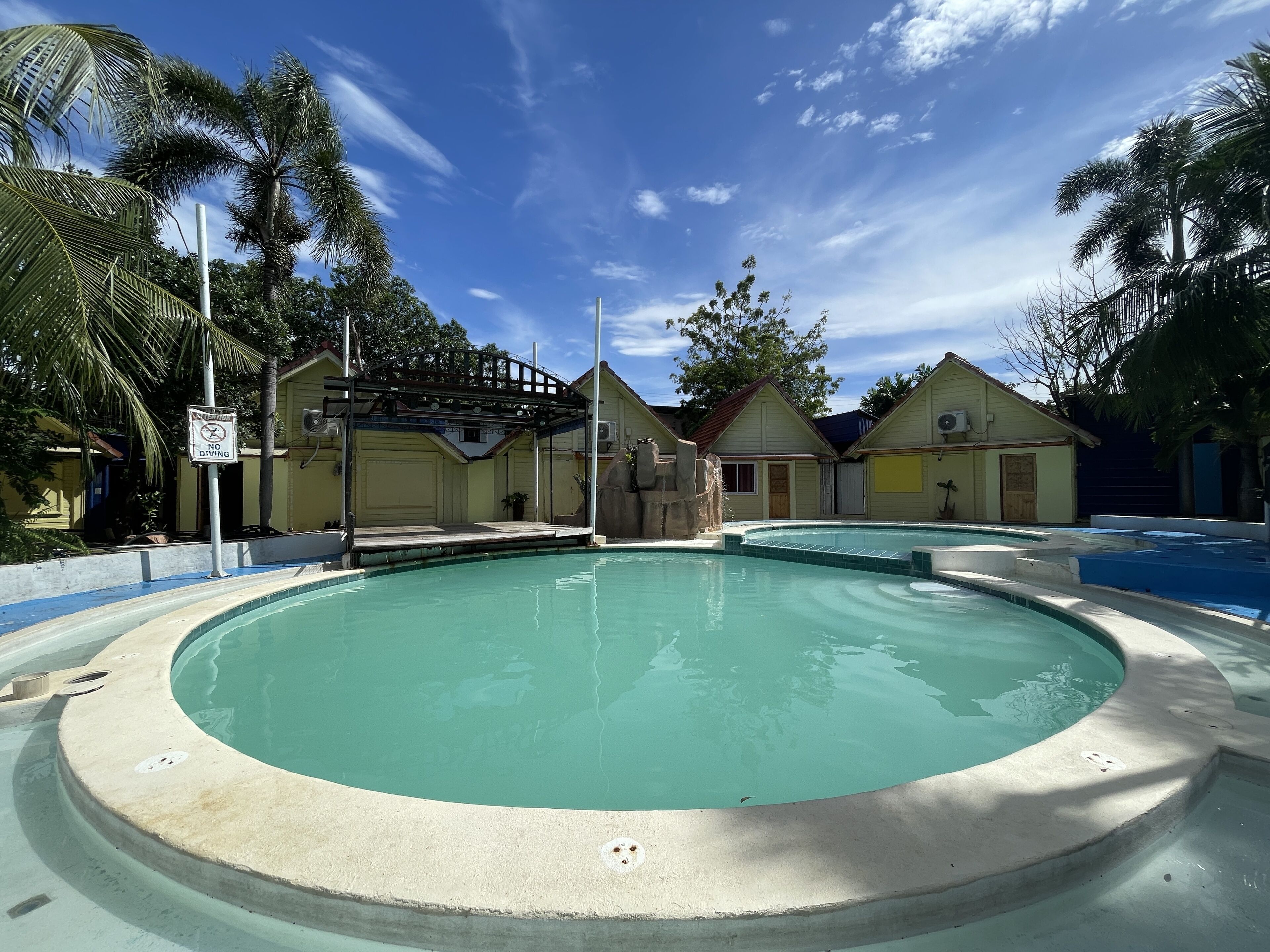 Bereich eines Pools mit einem 'No Diving'-Schild, umgeben von Palmen und blauem Himmel.