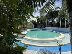 A multi-level swimming pool with clear water, surrounded by palm trees and a building in the background. - MAH Resort by Cocotel (Parañaque)