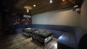 Una habitación con un sofá azul, dos otomanas negras con diseños blancos, techo de madera y un equipo de aire acondicionado.