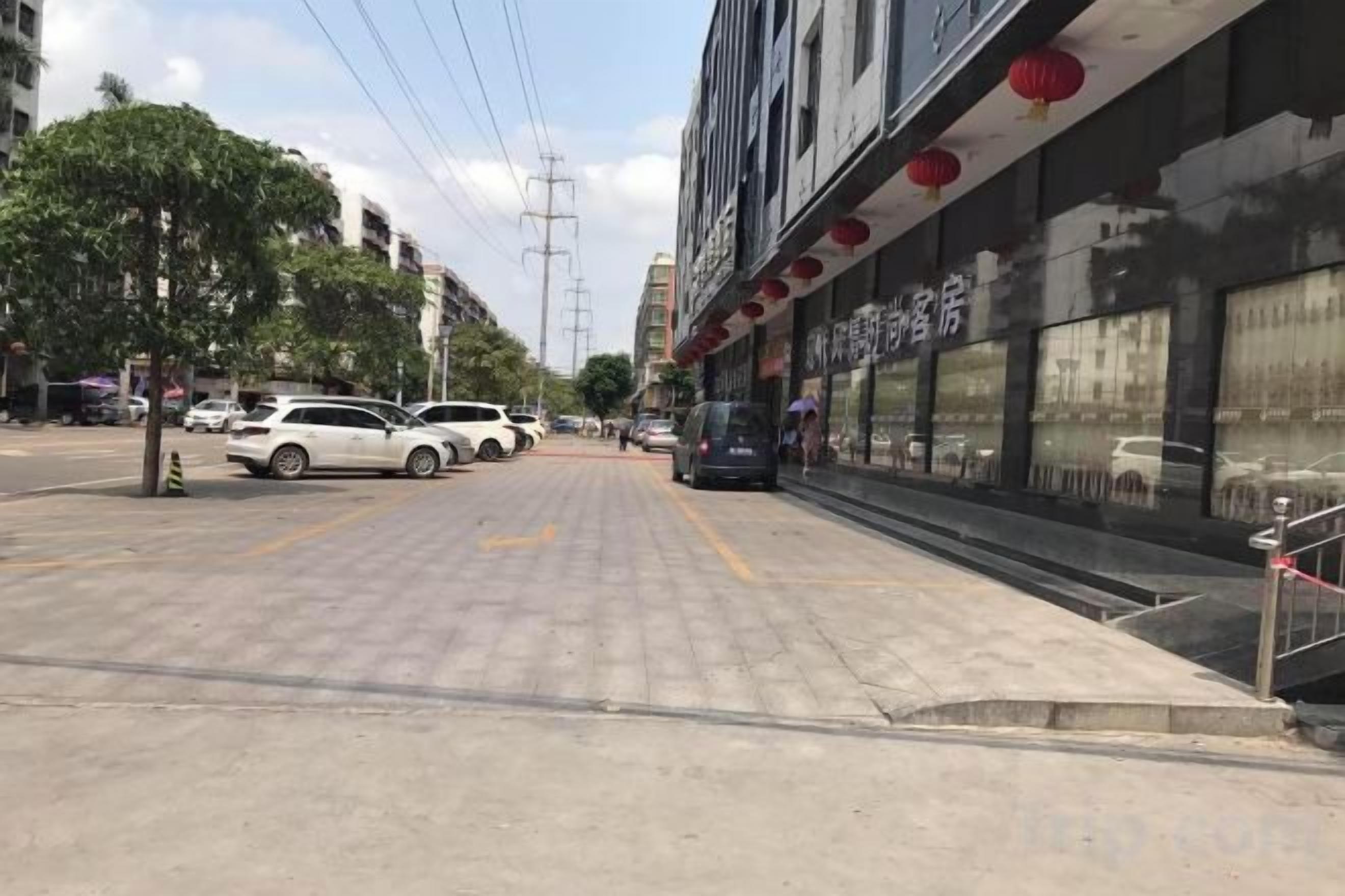 A street view with a building featuring a storefront with red lanterns, a sidewalk, and parked cars.