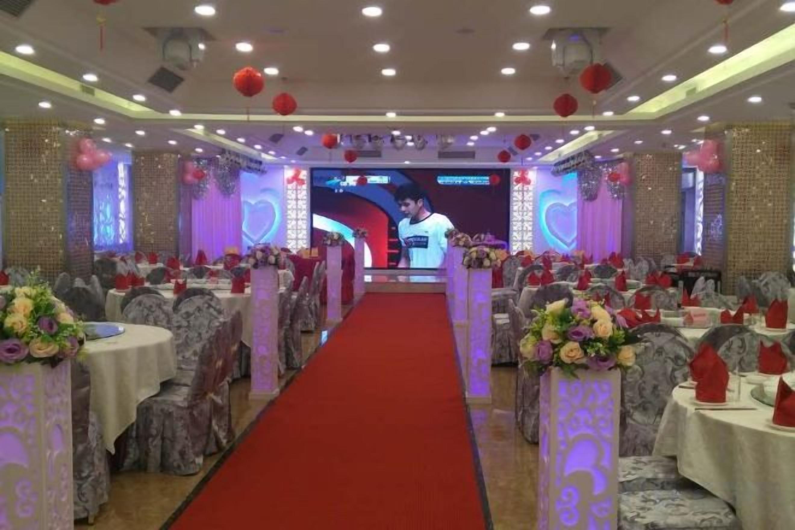 A banquet hall with round tables, a red carpet aisle, and a stage with a large screen.