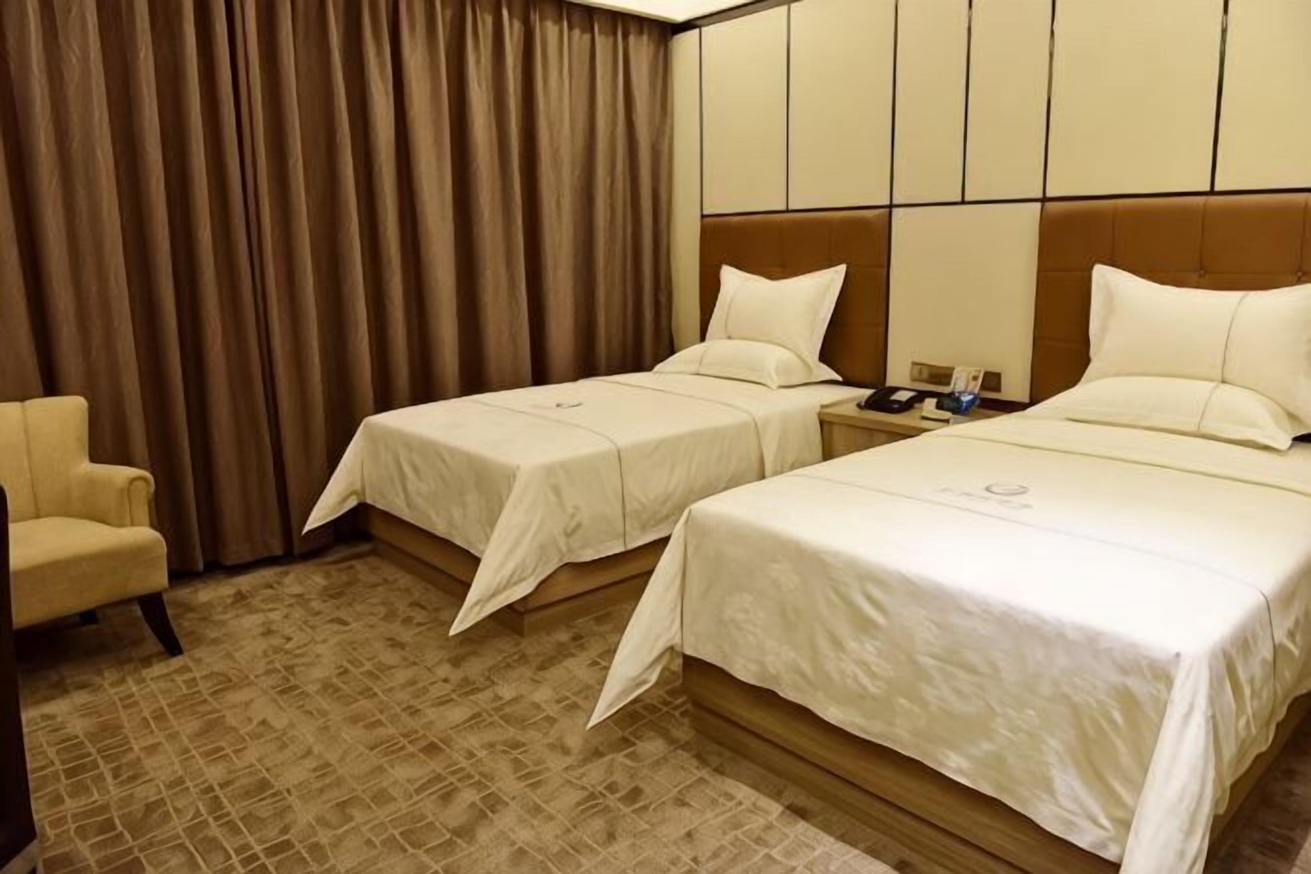 A hotel room with two beds, a chair, and a curtain.