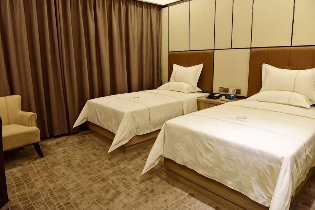 A hotel room with two beds, a chair, and a curtain.