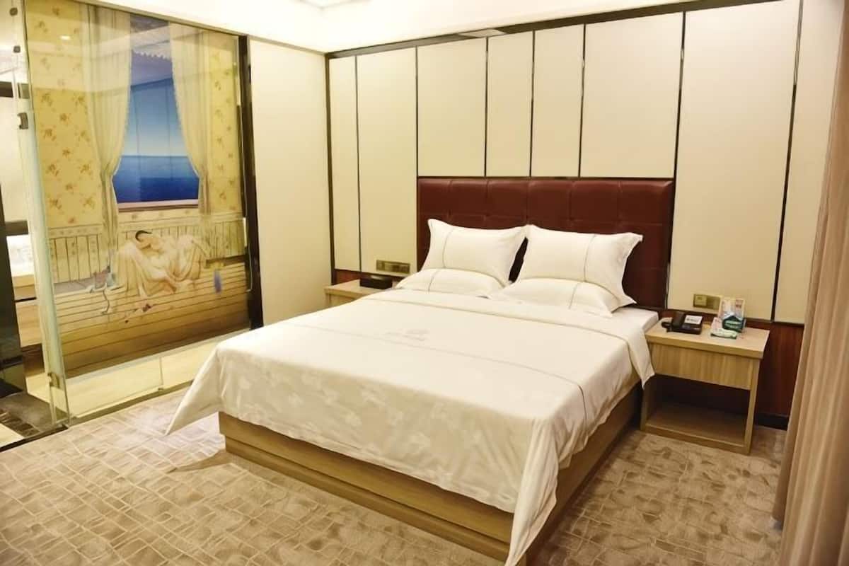 A hotel room with a large bed, a nightstand, a glass partition, and a view of a balcony.