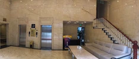 A lobby with marble flooring, a sofa, a table, an elevator, and a staircase.