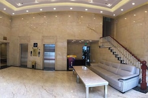Eine Empfangshalle mit Marmorböden, einer Couch, einem Tisch, einem Aufzug und einer Treppe.