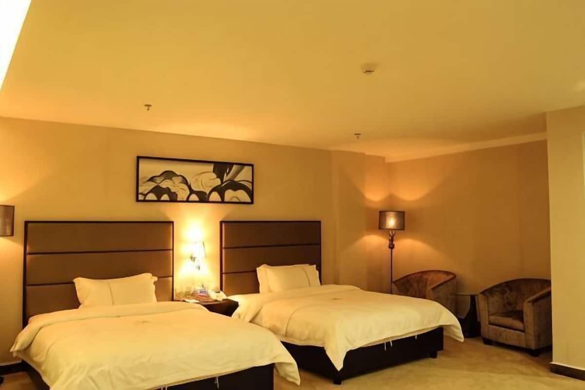 Ein Hotelzimmer mit zwei Betten, einem Nachttisch, einer Lampe, einem Sessel und einem Bild an der Wand.