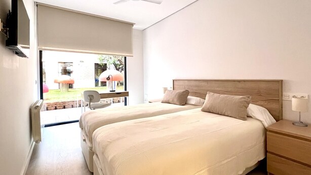 Quarto moderno com duas camas, ventoinha no teto e vista para o exterior.