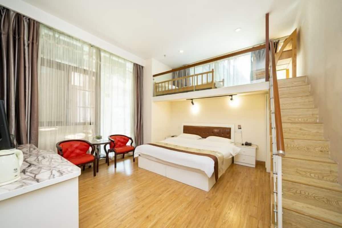 Habitación de hotel con cama, escritorio, silla, escalera y balcón.