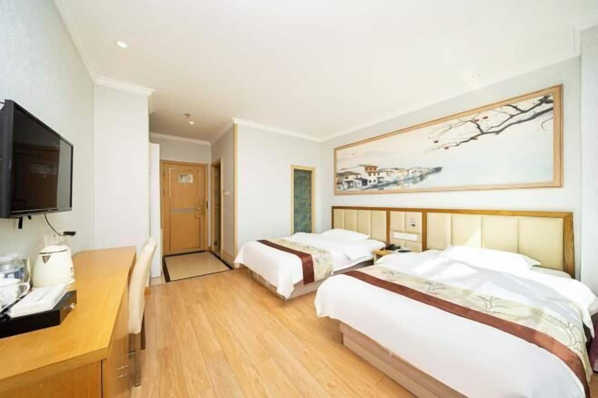 Habitación de hotel con dos camas, un escritorio de madera, un televisor y un cuadro en la pared.