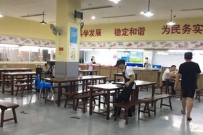 A cafeteria with tables and chairs, a counter with a person serving food, and a wall with text. - Hanshe Ligong Hotel (Shanghai Dahongqiao National Convention and Exhibition Center) (Shanghai)