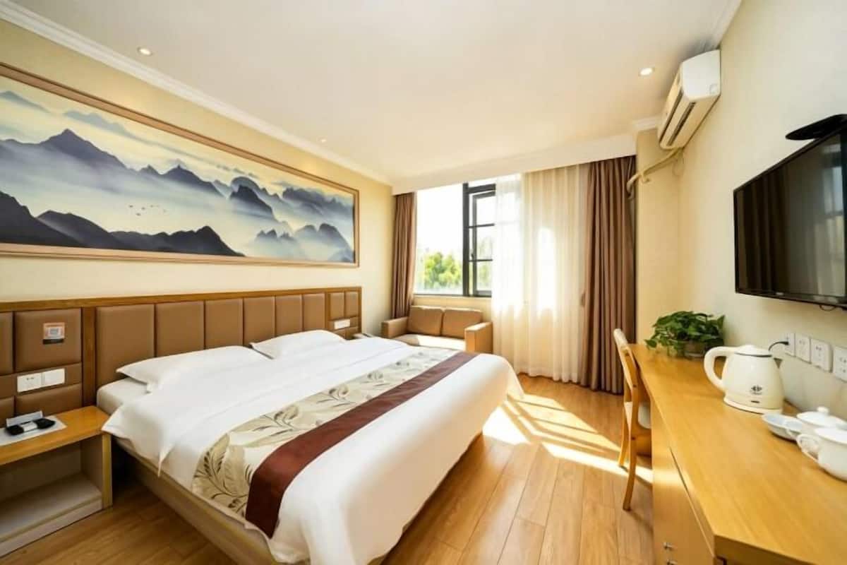 Habitación de hotel con una cama grande, un escritorio con hervidor, un televisor de pantalla plana y un cuadro en la pared.