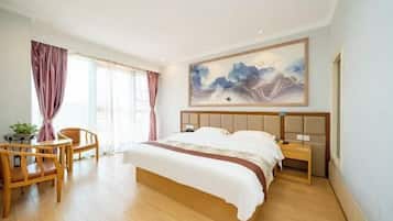 Ein Hotelzimmer mit einem großen Bett, einem Holz-Kopfstück, einem Nachttisch, einem Sessel, einem Schreibtisch und einem großen Gemälde an der Wand.