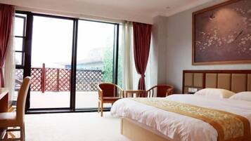 Habitación de hotel con cama, escritorio, sillas y un ventanal con cortinas.